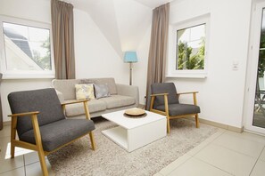 Ein modernes Wohnzimmer mit einer Couch, zwei Sesseln, einem Couchtisch und einer Lampe.