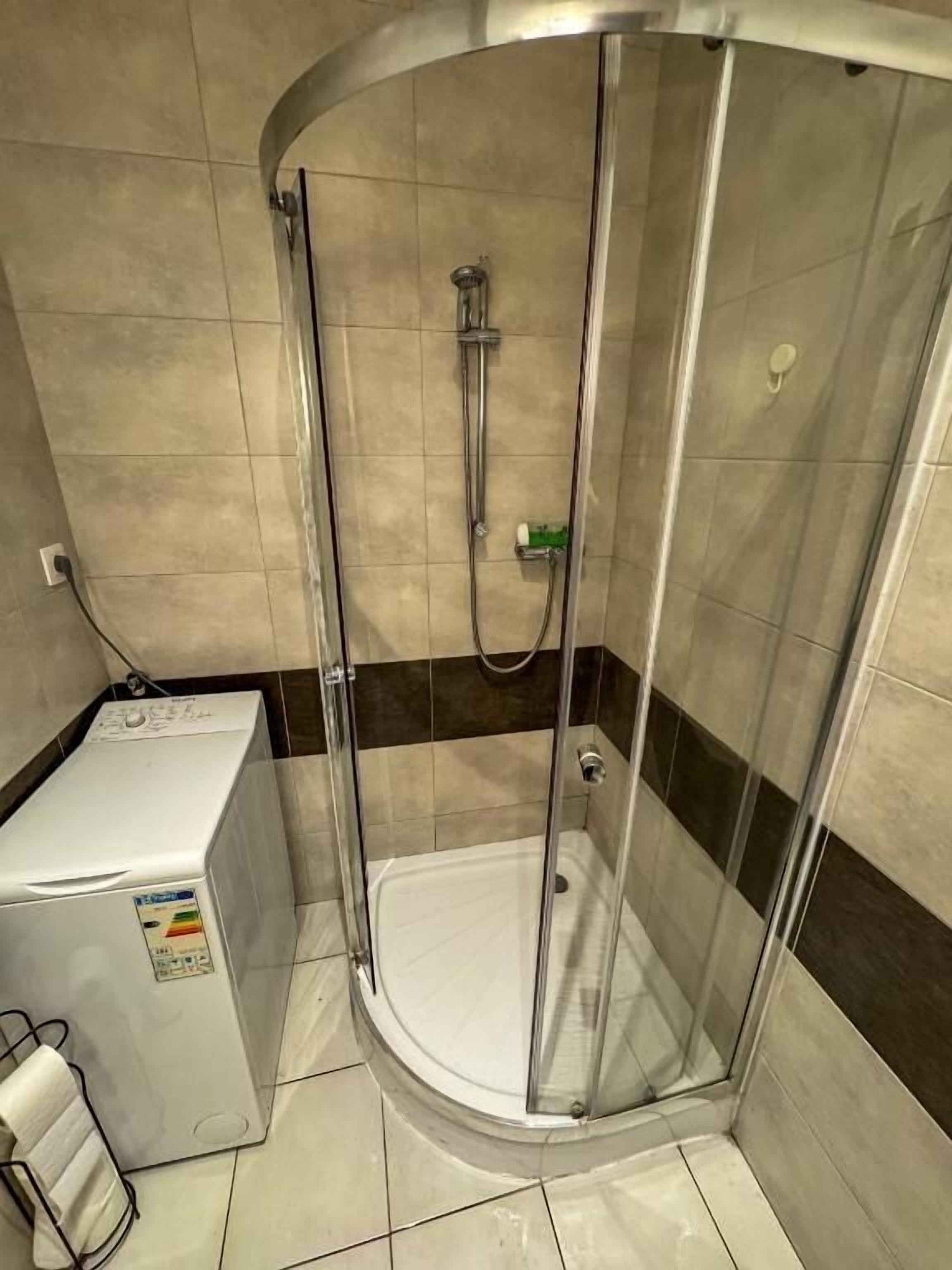 A shower enclosure with a glass door, a handheld showerhead, and a wall-mounted faucet.