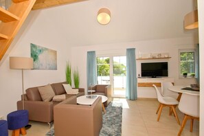 A modern living room with a sofa set, a coffee table, a TV, and a dining area with chairs. - Beachfront apartment with balcony, use of swimming pool and sauna - Rex Rugia H-1010 - (Mönchgut)