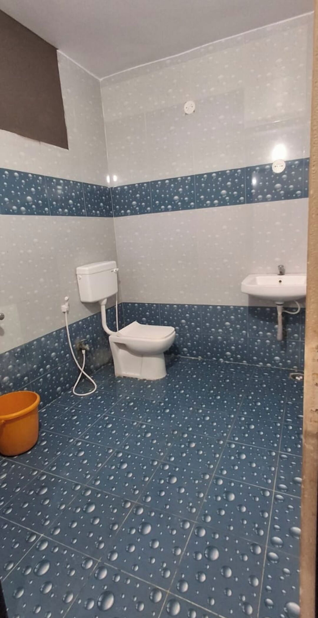 Un baño con inodoro, lavamanos y piso de baldosas azules.