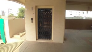 Ein Gebäudeeingang mit einem Metallgitter, einer kleinen Treppe, die zu einem Balkon führt, und einer schlichten Außenwand.