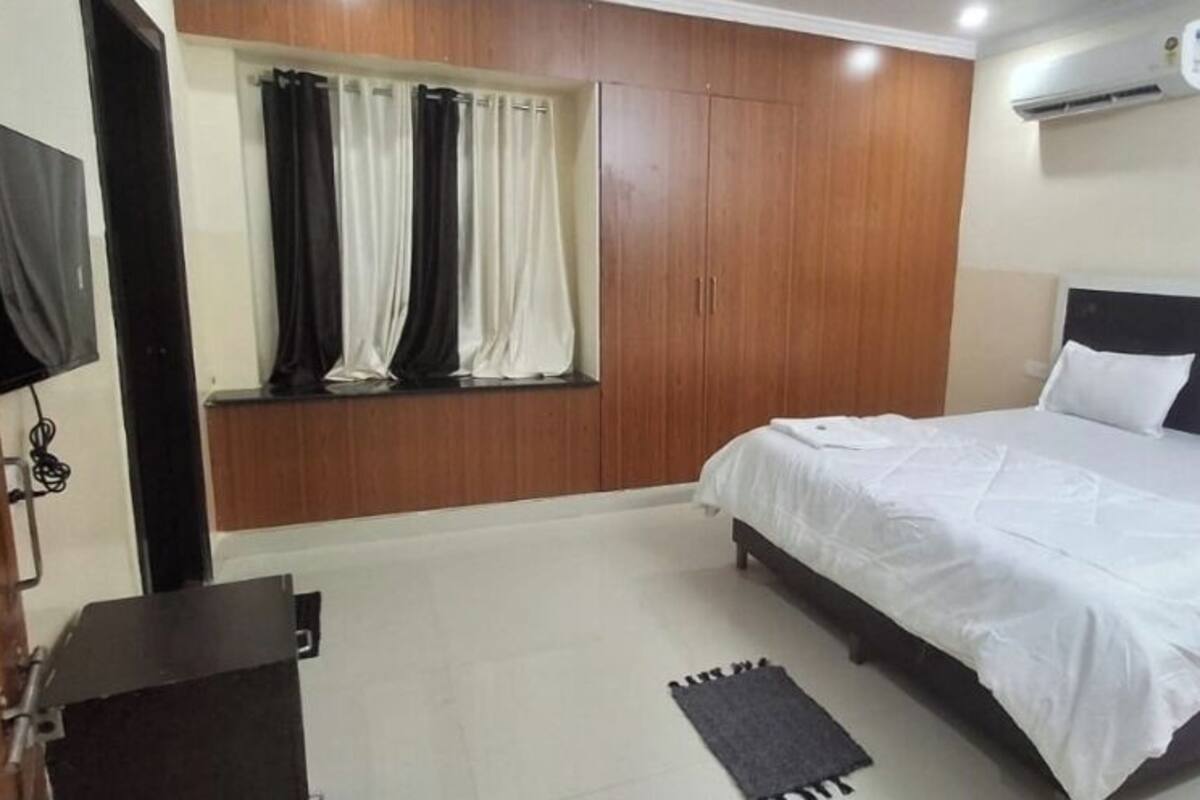 A bedroom with a bed, a TV mounted on the wall, a wardrobe, and a window with curtains.