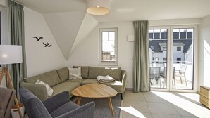 En moderne stue med en hjørnesofa, et rundt sofabord og udsigt til balkonen.