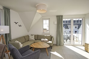 A modern living room with a sectional sofa, a round coffee table, and a view of the outside balcony. - Beachfront apartment with balcony, use of swimming pool and sauna - Rex Rugia H-1010 - (Mönchgut)