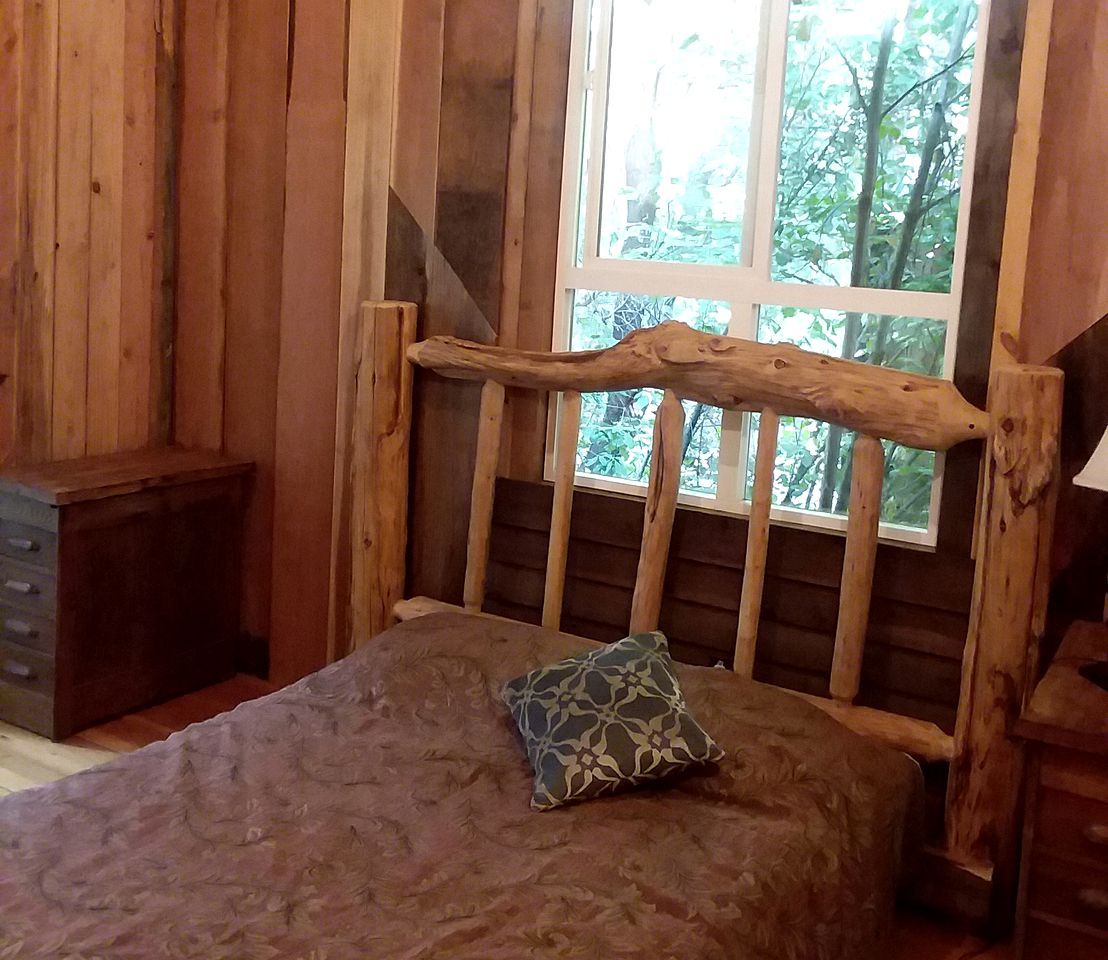 Une pièce dans un chalet en bois, comprenant un lit, une fenêtre et un petit meuble en bois.