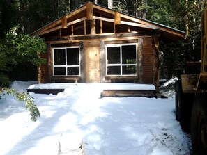 A wooden cabin with a front porch, large windows, and a snow-covered ground. - Rustic Shamballa Cabin near Tahoe National Forest, California (Nevada City)