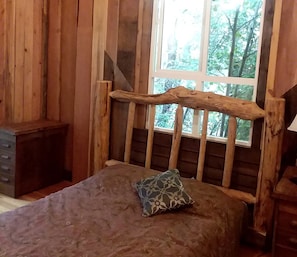 A wooden cabin room with a bed, a window, and a small wooden cabinet.