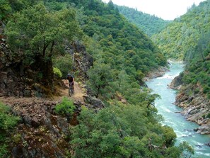 Ciclista de montaña en un sendero pedregoso, con un río al fondo.