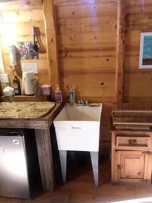 A wooden cabin interior with a sink, a small refrigerator, and a wooden cabinet.