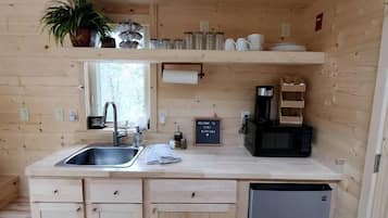 A compact kitchen with wooden cabinets, a sink, a coffee maker, and a small refrigerator.