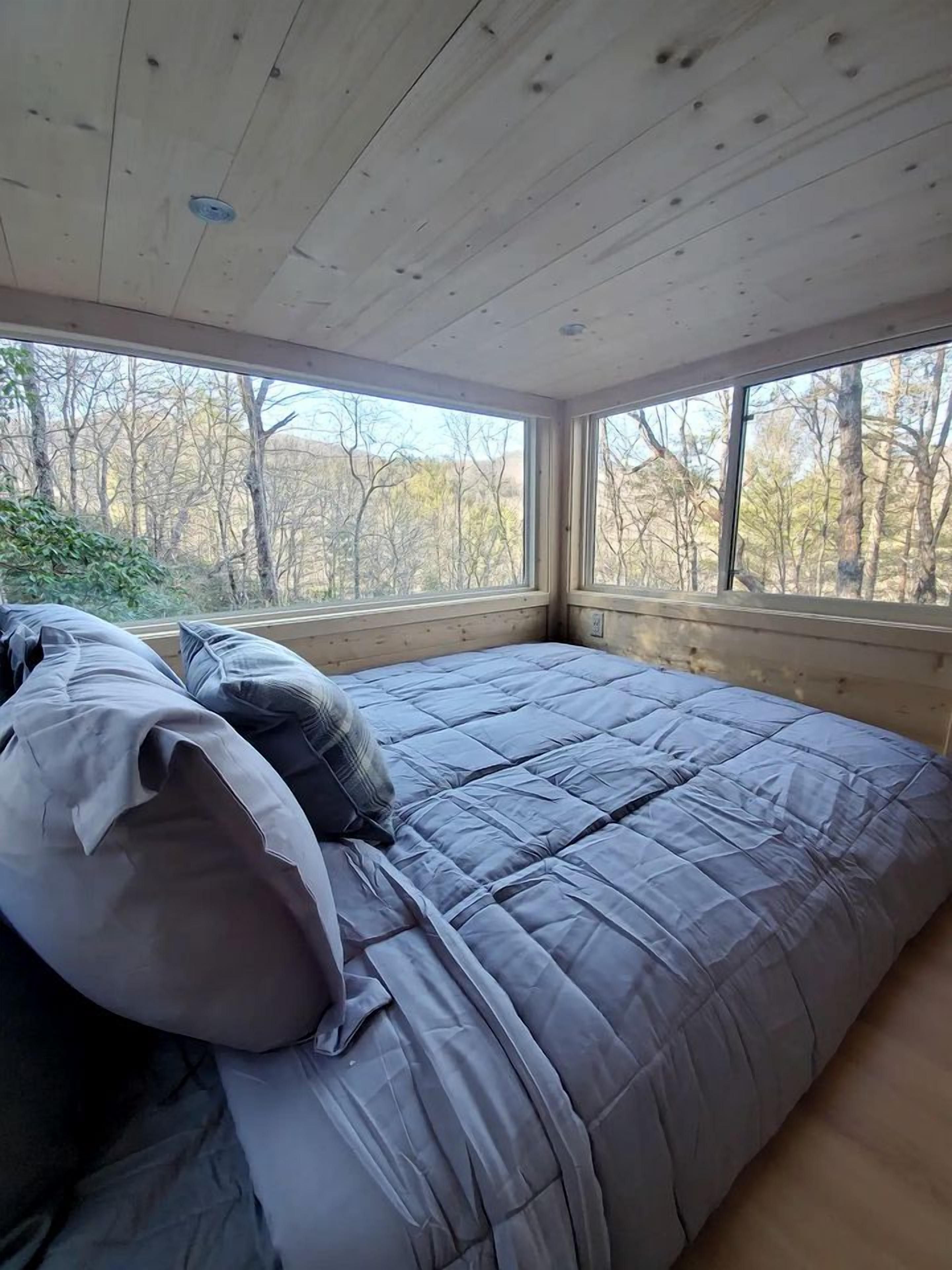 Une chambre à coucher avec un grand lit, un plafond en bois et des fenêtres donnant sur une forêt.