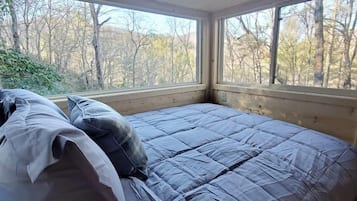Een slaapkamer met een groot bed, houten plafond en ramen met uitzicht op een bos.