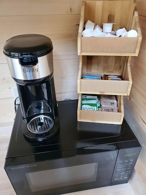 Une machine à café posée sur un four à micro-ondes, une étagère en bois avec des boîtes et un four à micro-ondes.