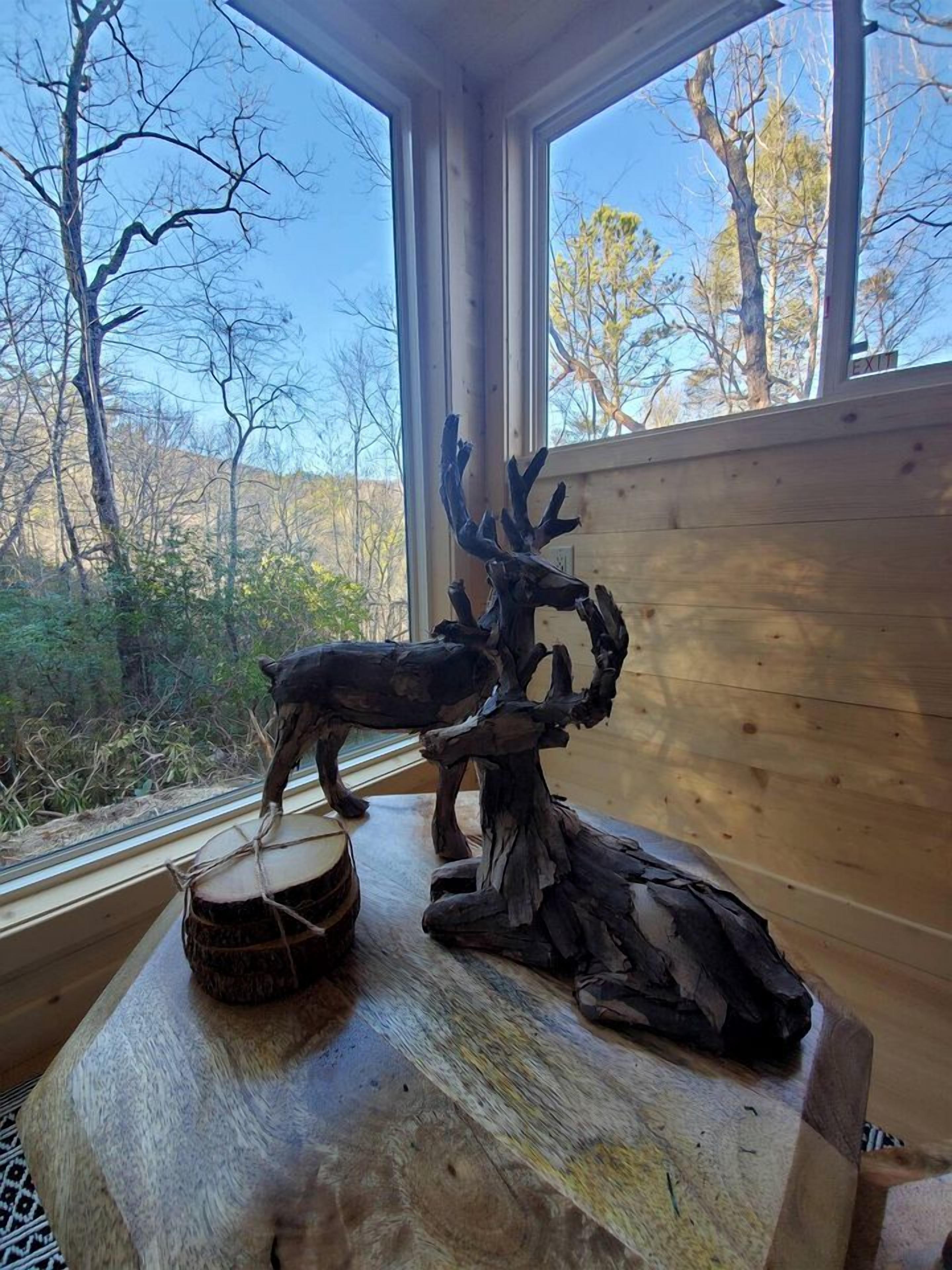 A wooden interior with a large window, a carved deer head, and a drum on a table.