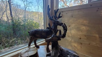 Un intérieur en bois avec une grande fenêtre, une tête de cerf sculptée et un tambour posé sur une table.