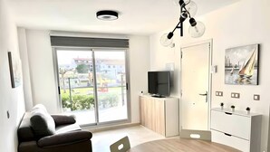 Una sala de estar moderna con sofá, mesa de comedor, televisor sobre un mueble bajo y un ventanal con vistas.