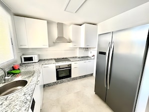 A modern kitchen with white cabinets, a stainless steel refrigerator, a microwave, and a granite countertop.