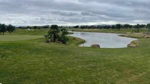 Un campo de golf con un estanque, árboles y un cielo nublado.