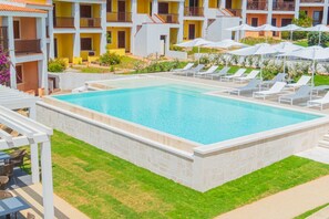 A swimming pool with lounge chairs and umbrellas, surrounded by a well-maintained lawn and a multi-story building with balconies. - Ideal for two people, the Mono Classic is the perfect choice for those seeking a cozy space with meticulous attention to detail. This unique space features an elegant double bed, a modern bathroom with shower, and a fully equipped kitchenette, designed f (Costa Serena - Palau)
