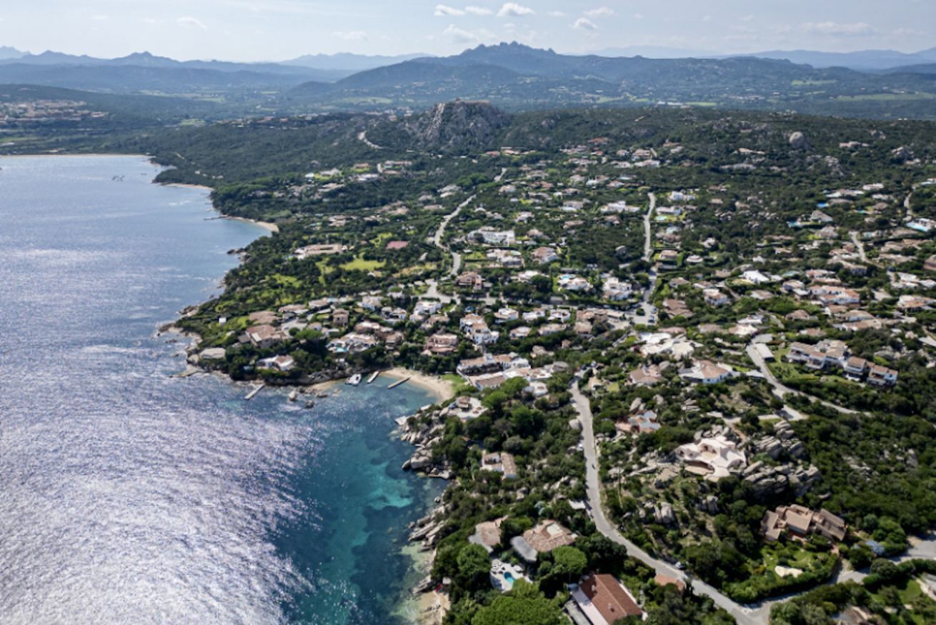 An aerial view of a coastal town with a mix of residential buildings, a beach, and a rocky coastline.