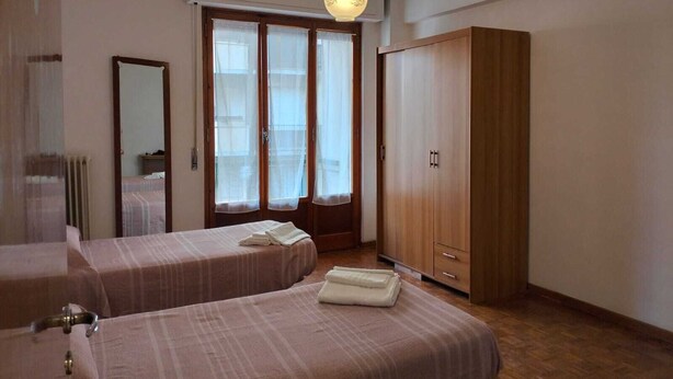 Ett hotellrum med två sängar, en garderob i trä, en stor spegel och ett fönster med gardiner.