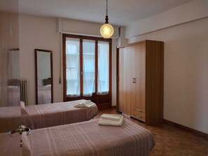 Quarto de hotel com duas camas, um guarda-roupa de madeira, um espelho grande e uma janela com cortinas.
