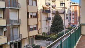 En flervåningsbostadsbyggnad med balkonger, ett grönt staket och ett träd på innergården.
