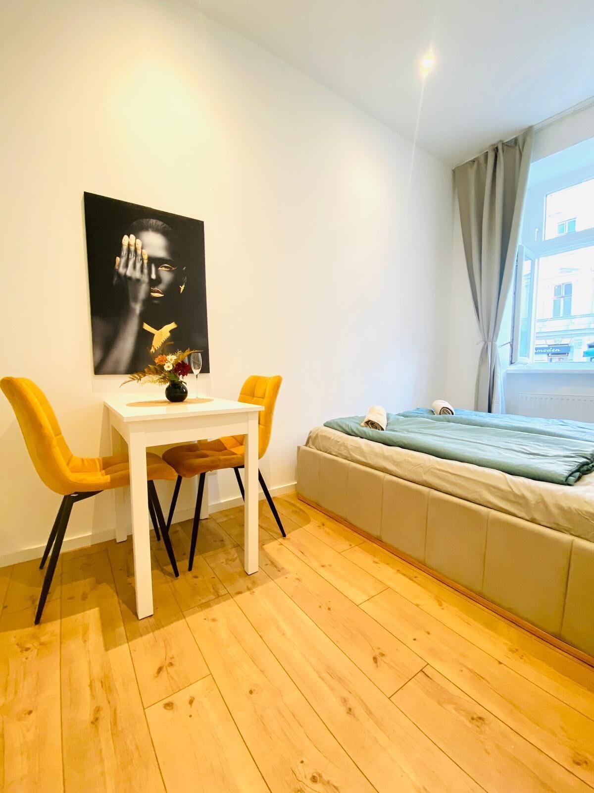 Una habitación pequeña con una cama, una mesita, dos sillas y un cartel en la pared.