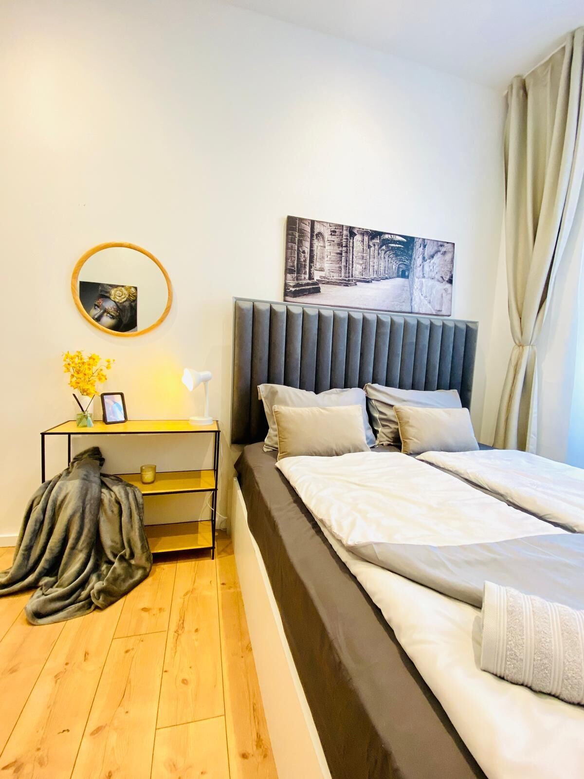 Un dormitorio moderno con una cama grande, una mesita de noche con lámpara, un cuadro enmarcado en la pared y una ventana con cortinas.