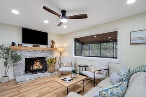 A living room with a stone fireplace, a ceiling fan, a large window, and a flat-screen TV. - Flat access - covered boat slip with dock-two car garage - year round water (Spring City)