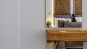 Ein Schlafzimmer mit einem großen Spiegel, einem Nachttisch aus Holz, einem Bett mit gemusterten Betttextilien und einem gewobenen Kopfteil.