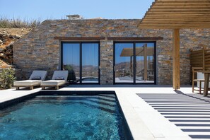 A stone building with a swimming pool, lounge chairs, and a view of the landscape. - Bonsai Luxury Villas Naxos (Glinado)