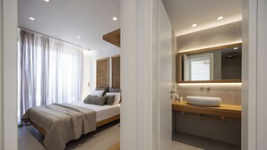 Ein modernes Schlafzimmer mit einem großen Bett, einem Nachttisch, einer eingebauten Ablage und einem großen Spiegel über dem Waschbecken.
