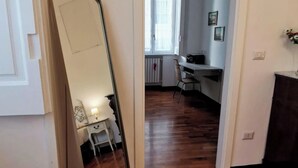 A room with a wooden floor, a desk, a chair, and a mirror reflecting part of the room. - Comfortable rooms in the heart of Vomero, just a few meters from the subway. (Napoli)