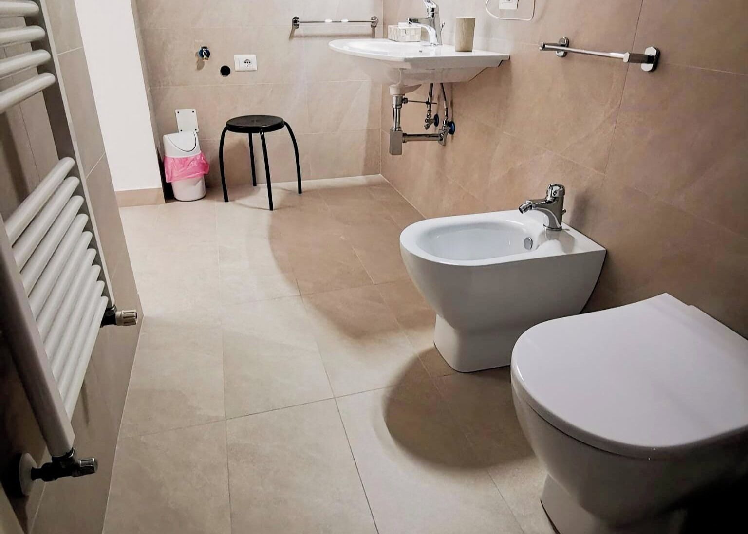 Ein Badezimmer mit einer Bidet, Toilette, Heizkörper, Waschbecken und einem kleinen Hocker.