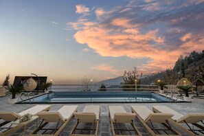 Un espace aménagé au bord de la piscine, avec des chaises longues, un panneau d’information et une vue sur les montagnes.