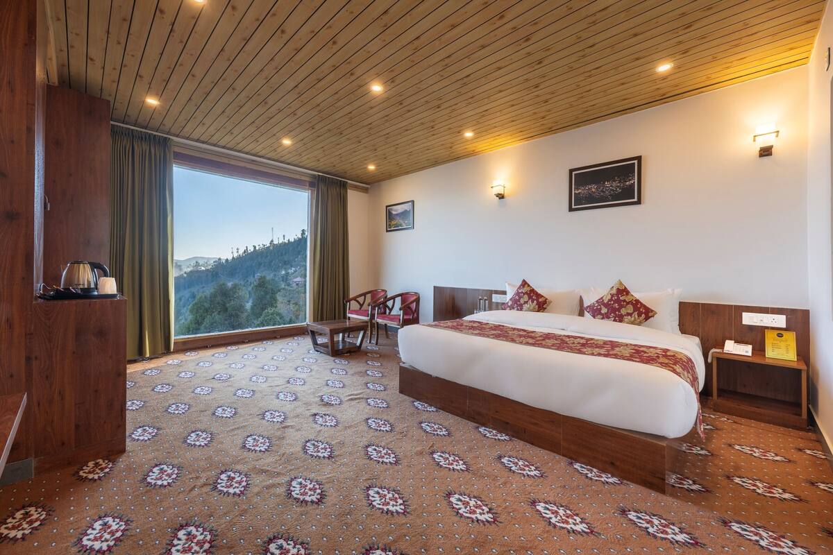 Une chambre d’hôtel avec un grand lit, un bureau, une chaise, une table de chevet et une vue sur l’extérieur.