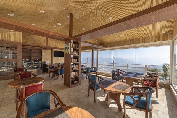 A modern indoor space with wooden ceiling and walls, featuring a bar area, seating with cushioned chairs, and a large window offering a view of the outdoors. - Echor KC Grand Kufri (Fagu)