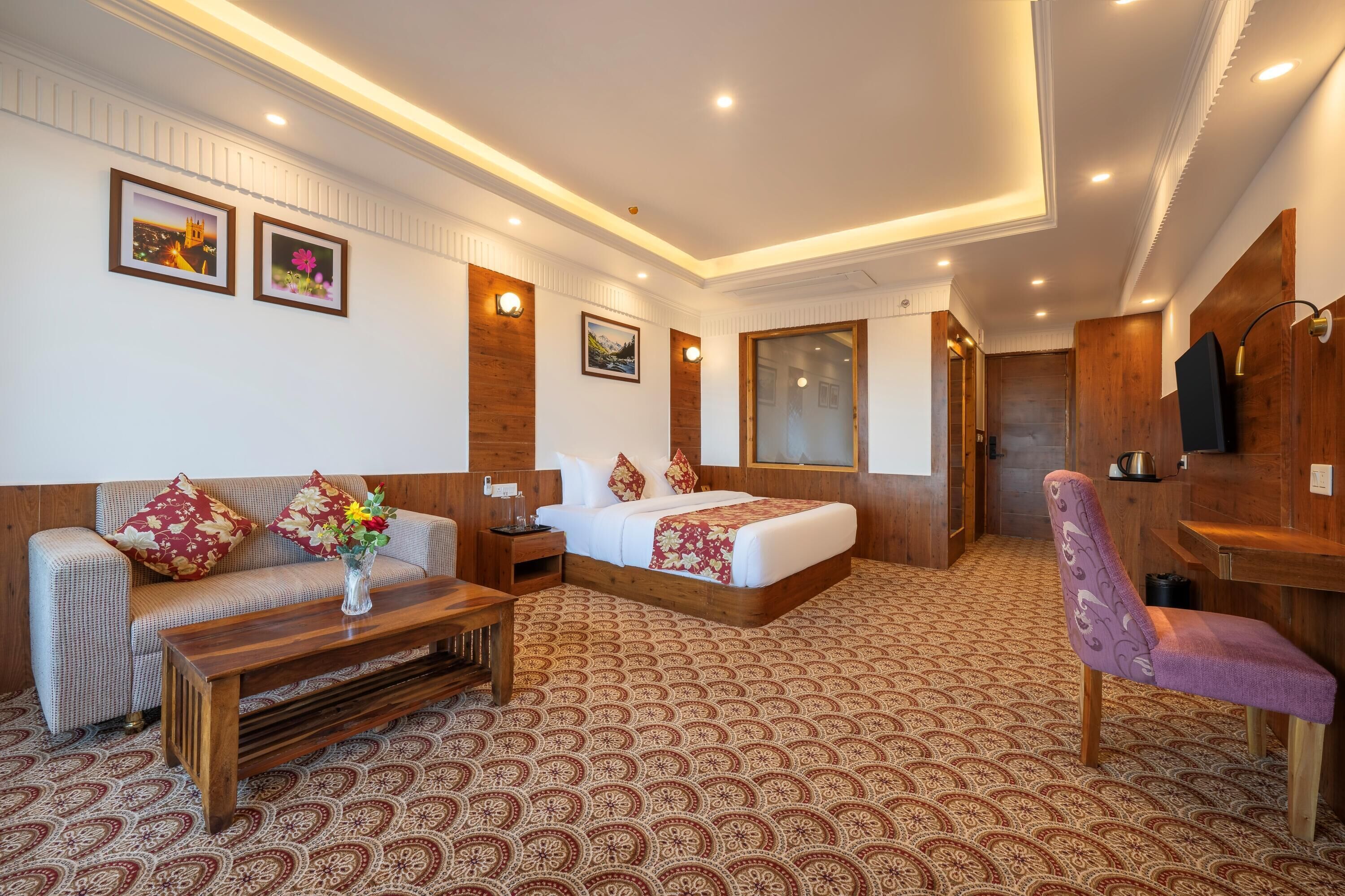 A hotel room with a bed, a sofa, a coffee table, a chair, and a TV.