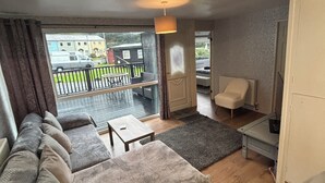 Una sala moderna con un sofá, una mesita y una silla. Hay un balcón con vistas a edificios y una furgoneta estacionada.