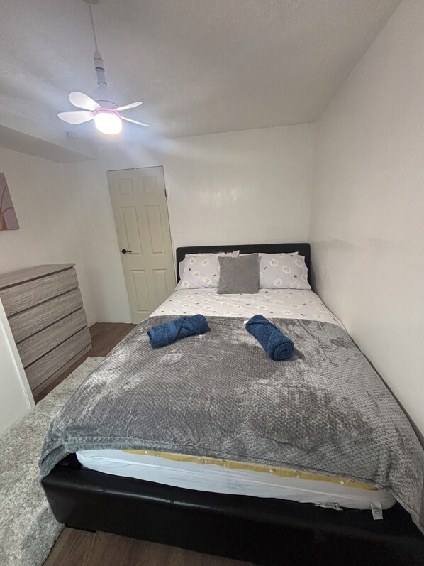 A small, neatly arranged bedroom with a single bed, a ceiling fan, and a door. - Edwards cabin (Caernarfon)