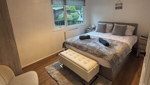 Un dormitorio con cama, mesita de noche, lámpara, ventana y una silla.
