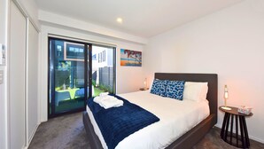 A hotel room with a bed, a small bedside table, a nightstand, a sliding glass door to a balcony, and a painting on the wall.