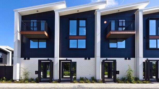 A modern multi-story residential building with balconies, large windows, and a brick facade.
