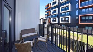A balcony with wicker furniture, a view of a modern building with multiple balconies, and a clear sky.