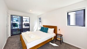 A bedroom with a bed, a bedside table, a lamp, and a window.