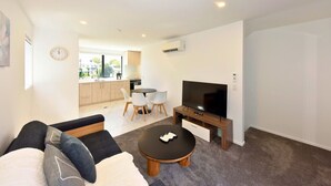 A modern living room with a sofa, a coffee table, a TV, and a dining area with chairs and a table.