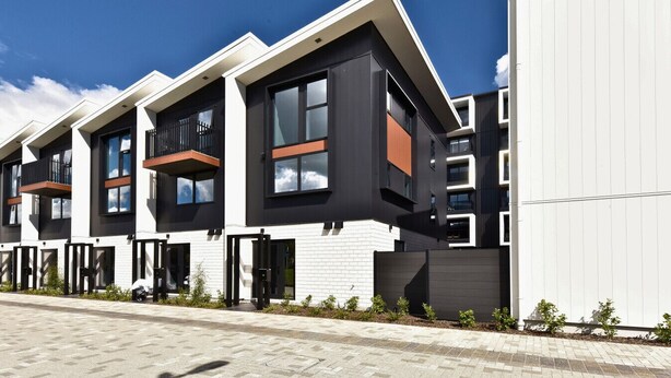 A modern residential building with a flat roof, large windows, and a balcony.