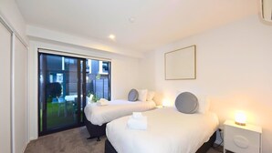 A hotel room with two beds, a sliding glass door to the outside, a bedside table with a lamp, and a large mirror on the wall. - Central 2BR Townhouse Close to Te Kaha Stadium (Christchurch)
