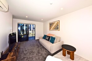 A living room with a sofa, a coffee table, a TV, and a sliding glass door leading to an outdoor area.
